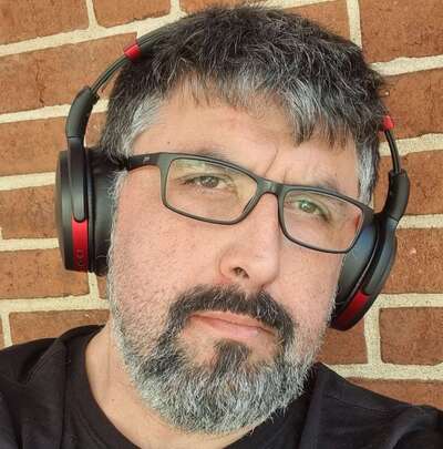 A photograph of Rob Norris, wearing glasses and headphones.